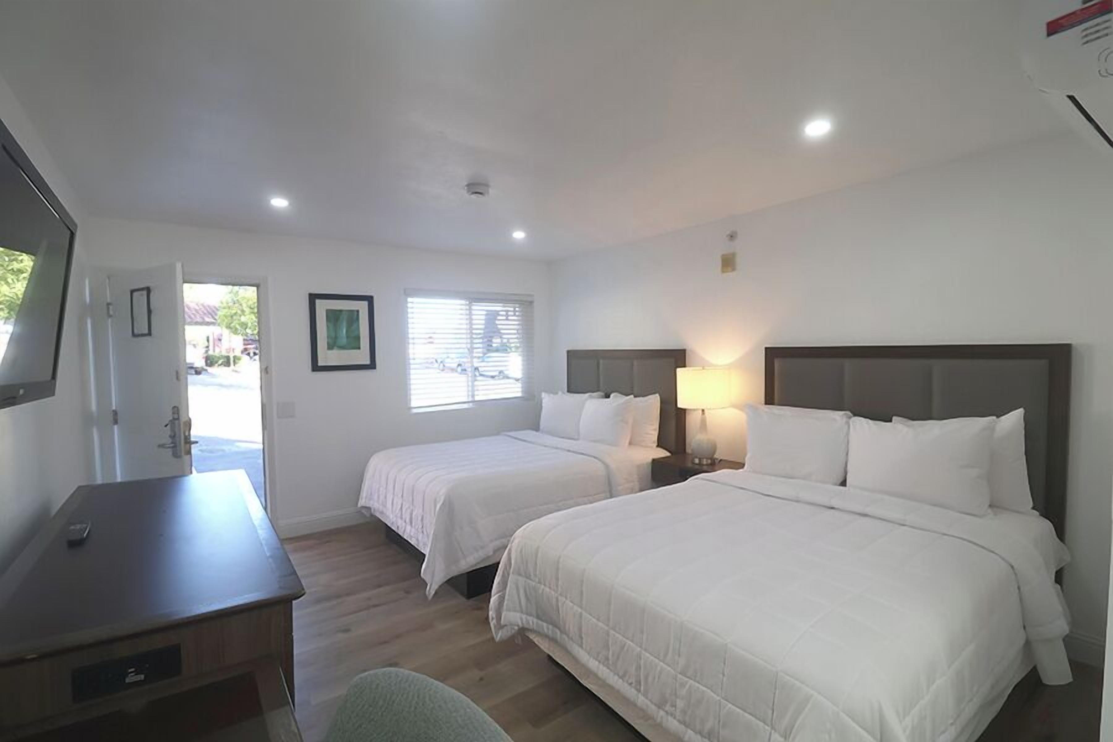 A hotel room with two beds, a desk, a chair, and a window with blinds.