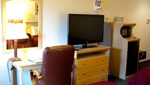 Et hotelværelse med en seng, et skrivebord med en computer, et fjernsyn, en mikrobølgeovn og en lampe.