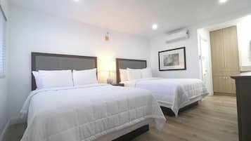 Een hotelkamer met twee bedden, een houten vloer, een kledingkast en een lijst met een afbeelding aan de muur.
