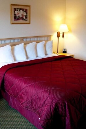 A hotel room with a bed, pillows, a nightstand, a lamp, and a framed picture on the wall. - Lamplighter Inn & Suites (San Luis Obispo)
