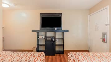 Ein Hotelzimmer mit zwei Betten, einem Fernseher, einer Minikühlschrank und einer kleinen Sitzecke.