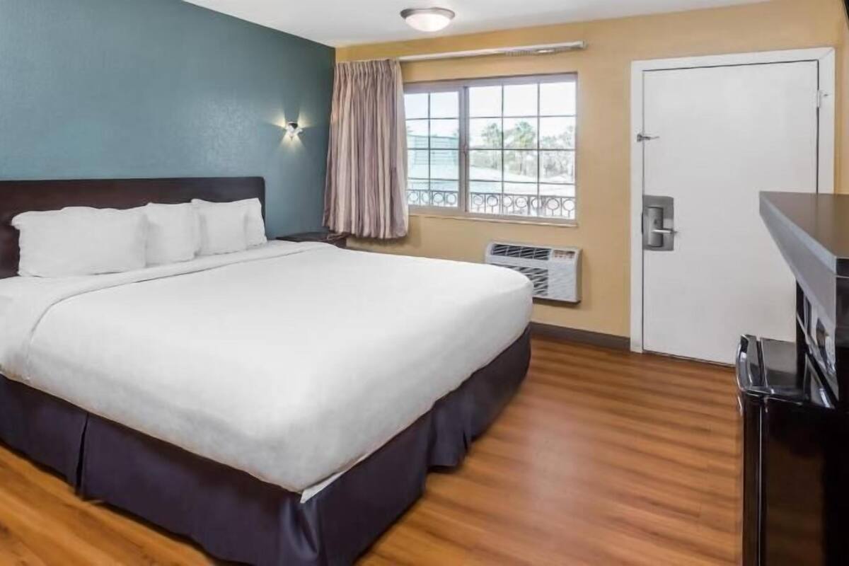 Ein Hotelzimmer mit einem großen Bett, einem Schreibtisch, einem Fenster mit Vorhängen und einer Klimaanlage.
