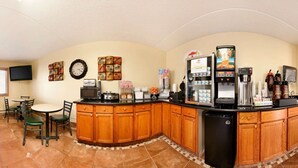 A kitchen area with a bar, dining tables, and chairs. There are various appliances and a refrigerator. - Super 8 by Wyndham West Fargo Main Ave ND (West Fargo)