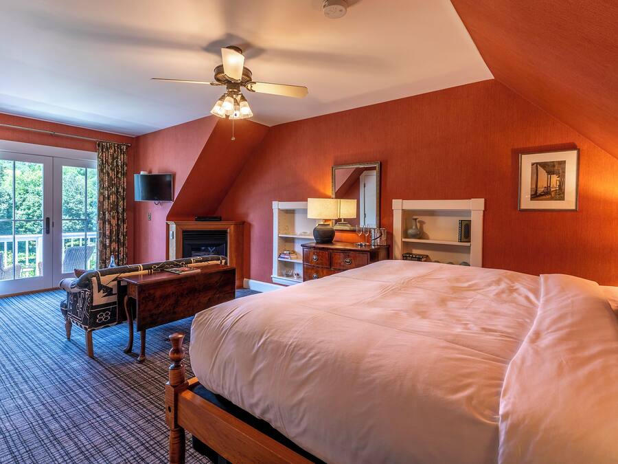 Une chambre avec un grand lit, un bureau, une chaise, une télévision et une cheminée.