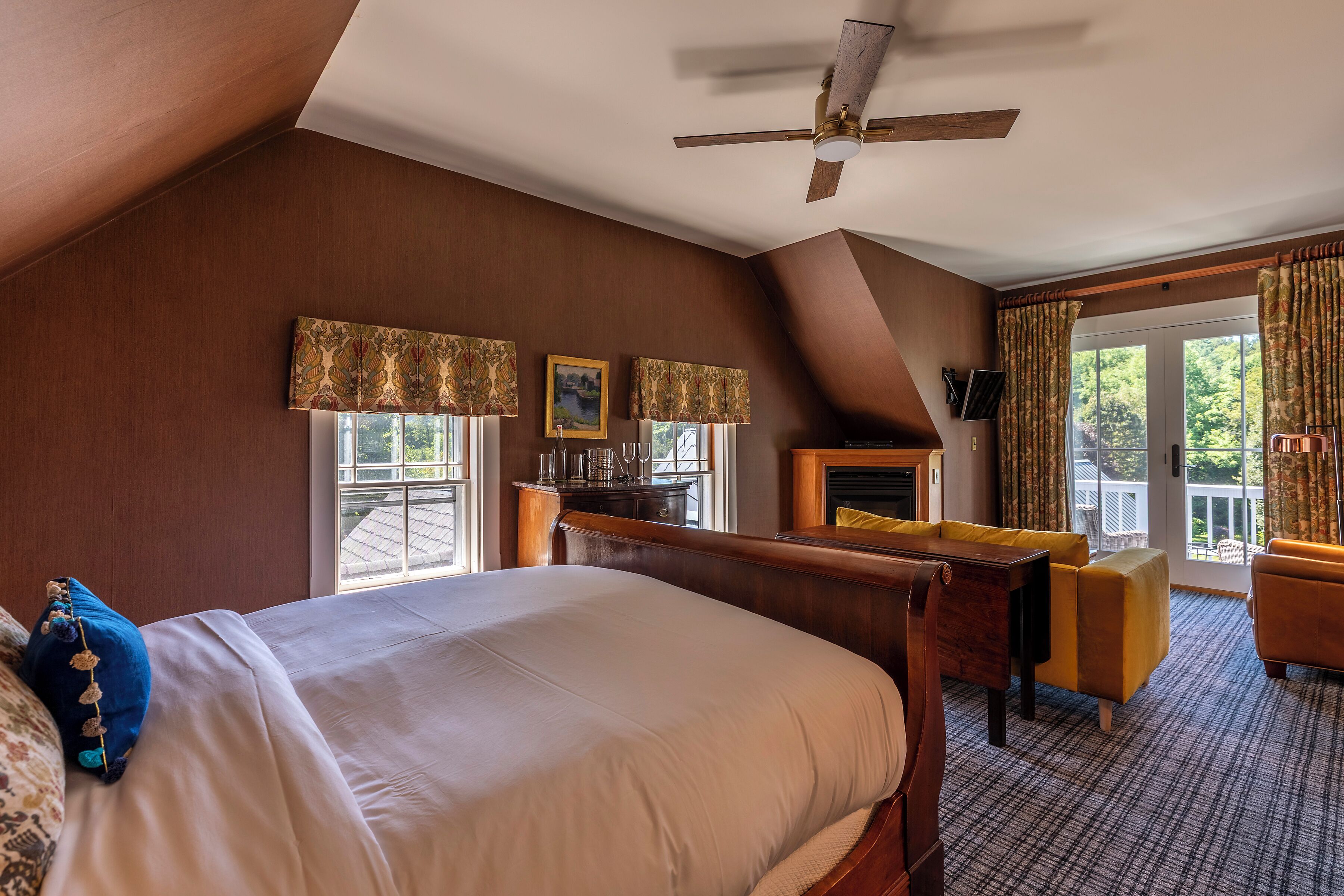 A hotel room with a large bed, a desk, a chair, a fireplace, and a view of the outdoors.