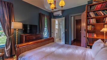 A bedroom with a large bed, a television, a bookshelf, and a window with curtains.
