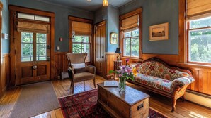 Una habitación acogedora con un banco de madera, una silla y un sofá. Cuenta con ventanas grandes de madera y un candelabro colgando del techo.