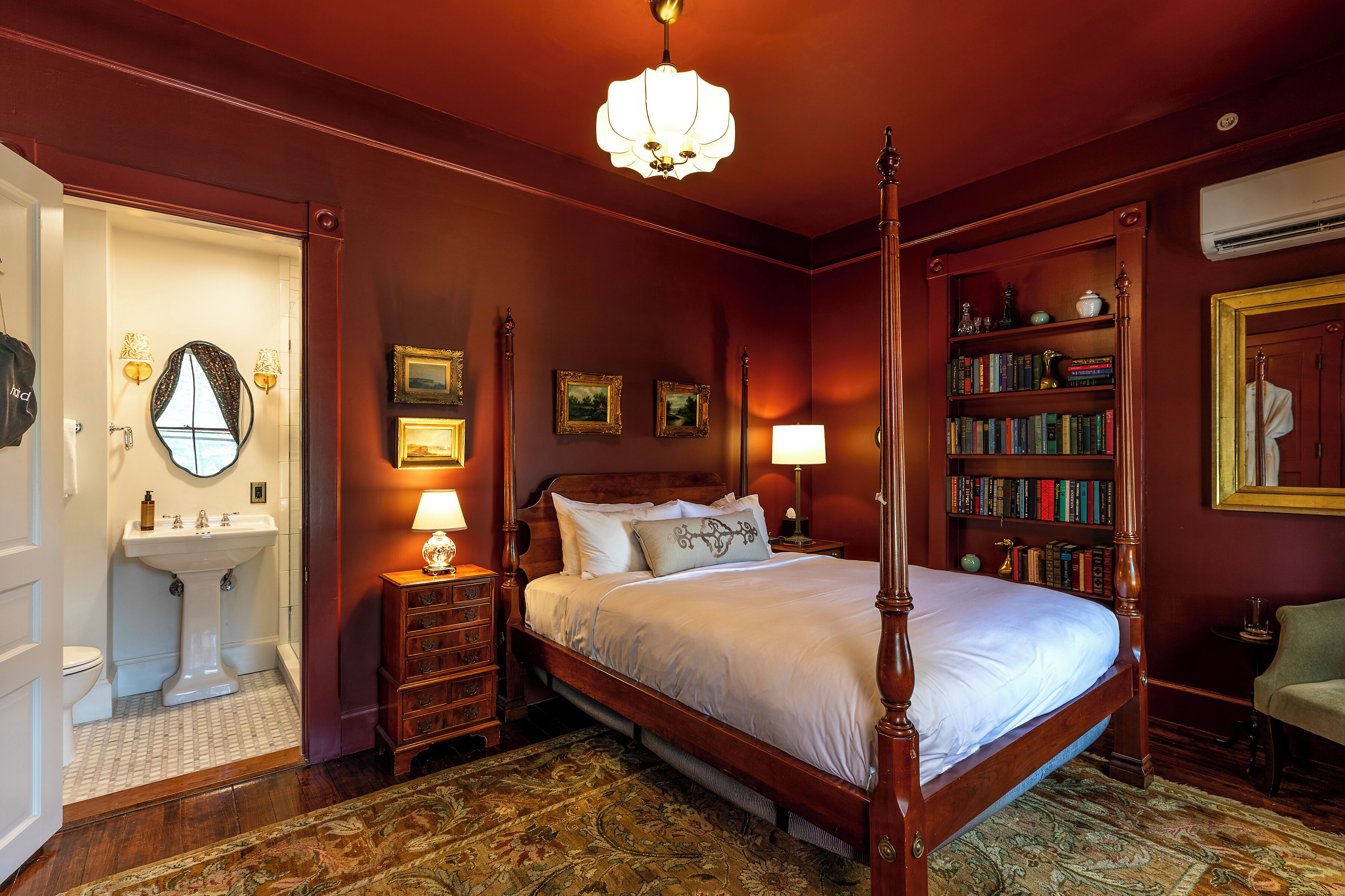 Une chambre à coucher avec un lit à baldaquin, une table de chevet avec une lampe, une bibliothèque et un grand miroir au-dessus du lavabo.
