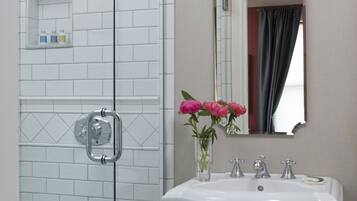Une salle de bain avec une douche à parois de verre, un lavabo blanc doté de deux robinets et un miroir au-dessus du lavabo.