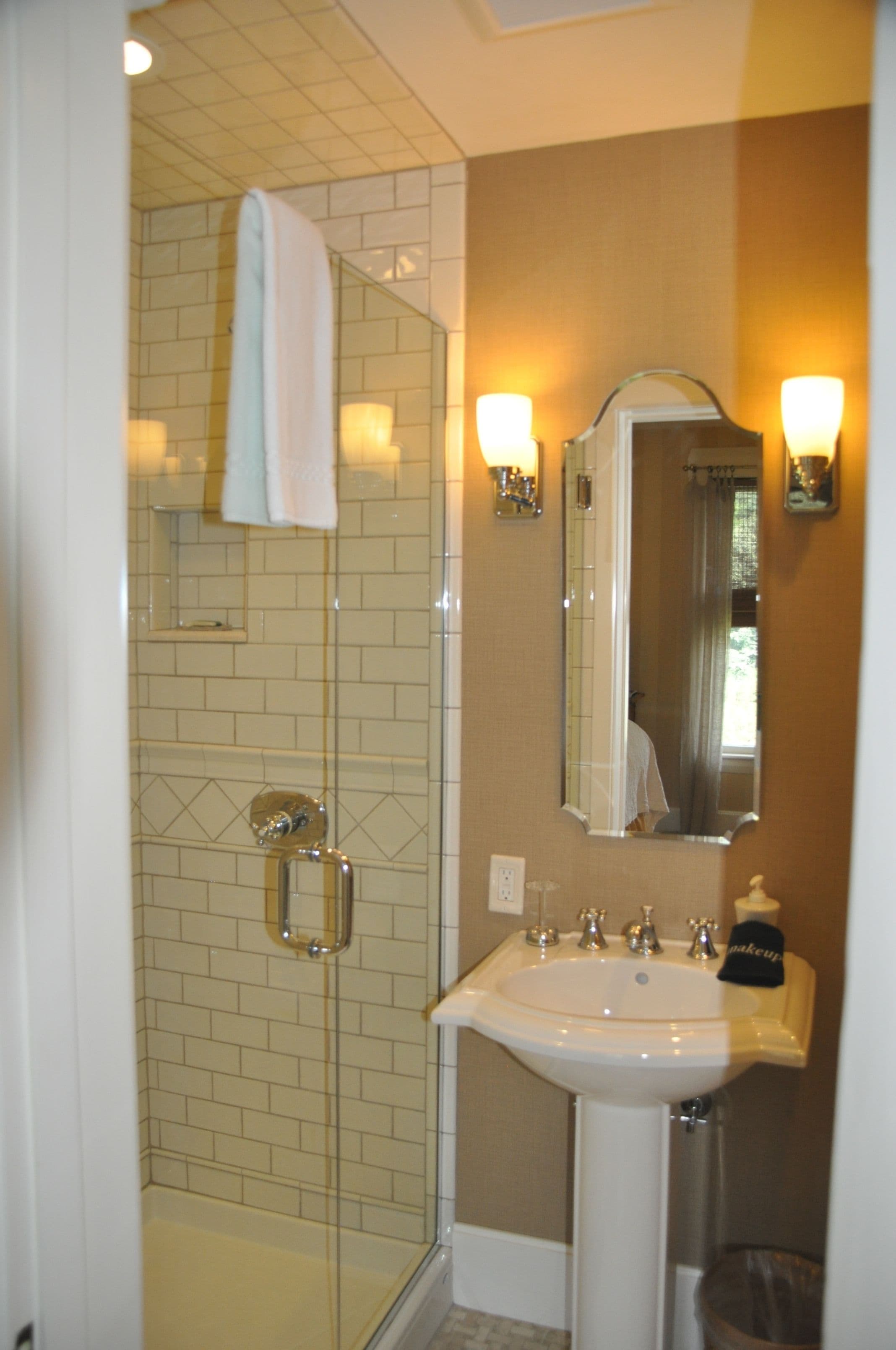 A bathroom with a glass-enclosed shower, a white sink, and a mirror with wall sconces.