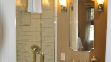 A bathroom with a glass-enclosed shower, a white sink, and a mirror with wall sconces.