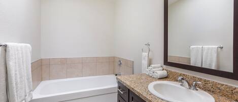 A bathroom with a bathtub, a sink, a mirror, and a towel rack.