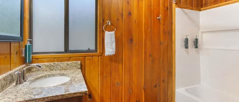 Ein Badezimmer aus Holz mit einem Granittisch, einem Fenster und einer Badewanne.