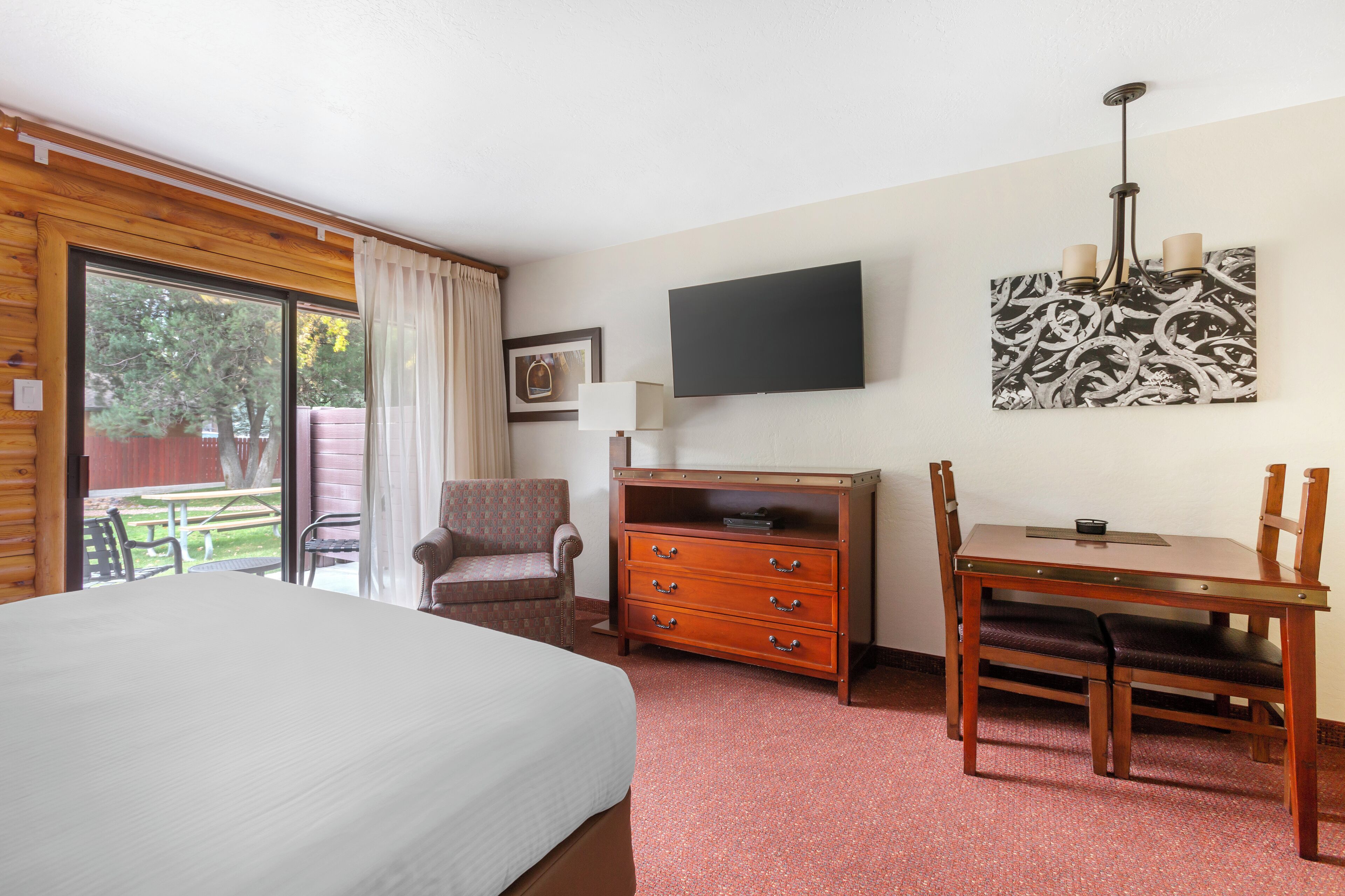 Una habitación de hotel con cama, escritorio, silla, cómoda, televisor y ventana con cortinas.