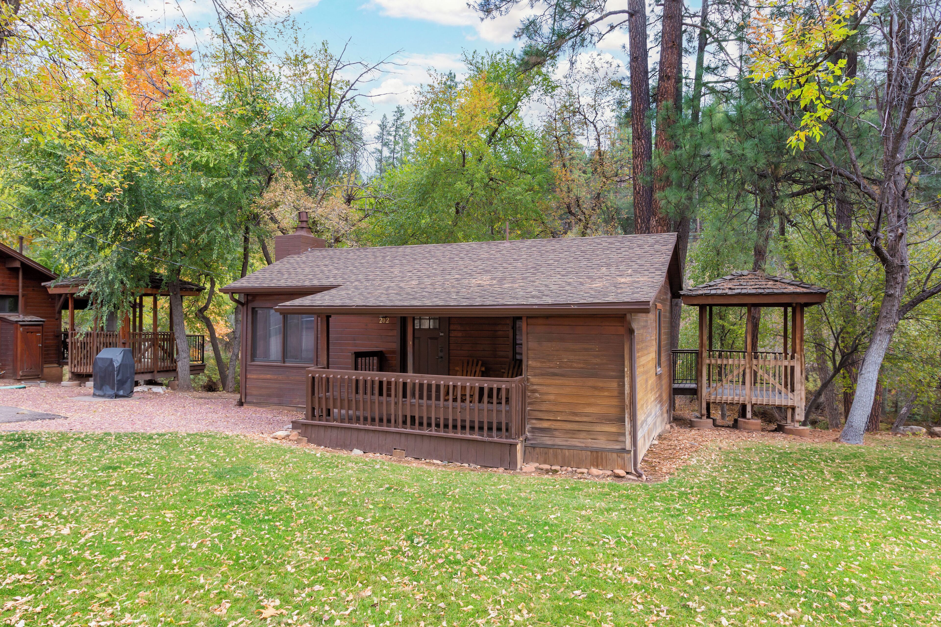 A rustic cabin with a porch, surrounded by trees and a grassy yard.
