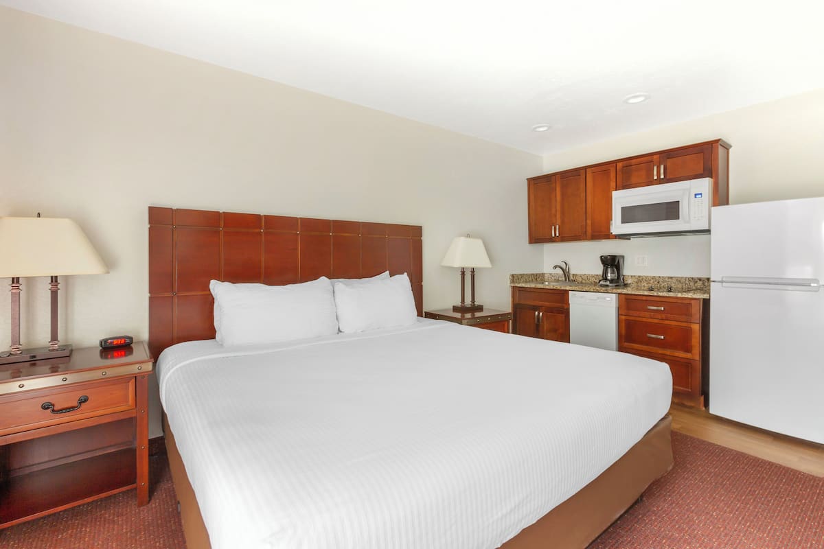 A hotel room with a large bed, wooden headboard, bedside tables with lamps, a microwave, a coffee maker, and a refrigerator.