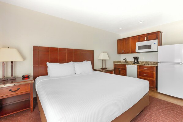 A hotel room with a large bed, wooden headboard, bedside tables with lamps, a microwave, a coffee maker, and a refrigerator.