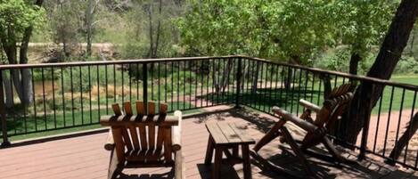 A wooden deck with two Adirondack chairs and a bench, surrounded by a metal railing.