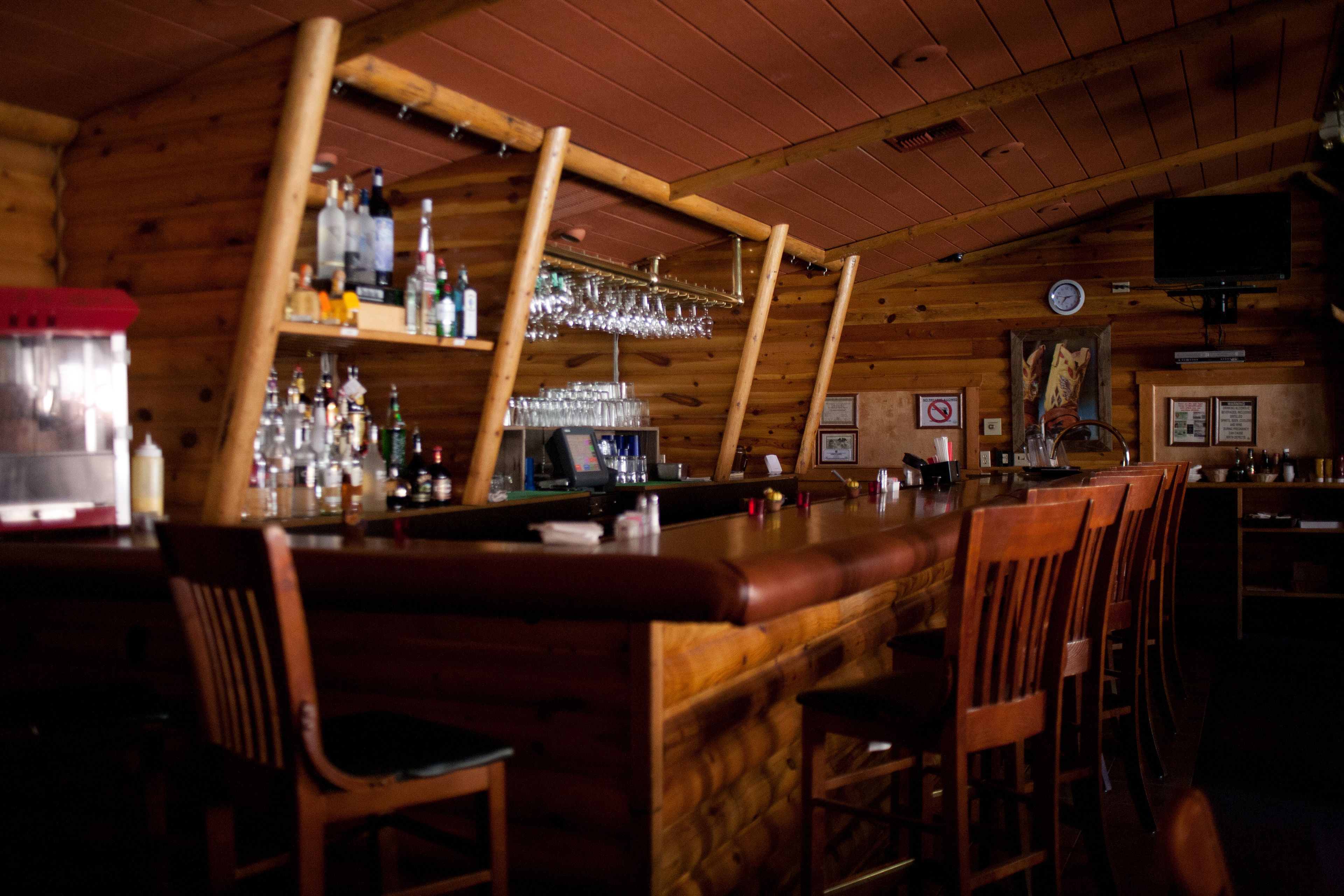Zona de bar con muebles de madera, estante con botellas y un reloj en la pared.