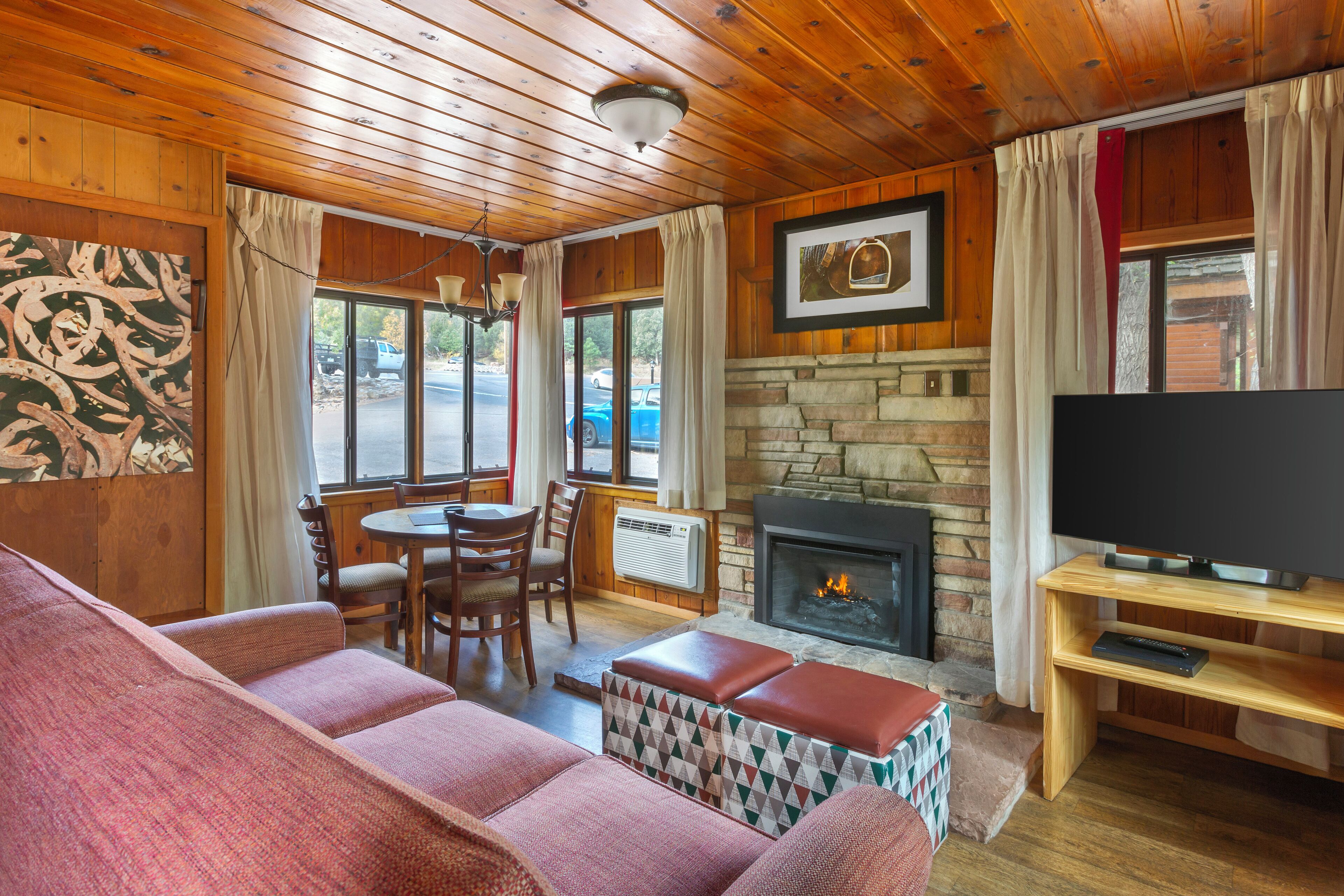 A cozy cabin interior with a stone fireplace, wooden ceiling, and a television on a wooden stand.