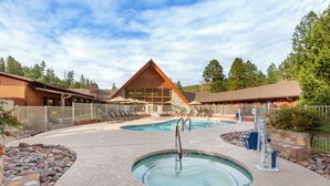 Un espace piscine doté d’un jacuzzi, de chaises longues et d’un bâtiment en bois en arrière-plan.