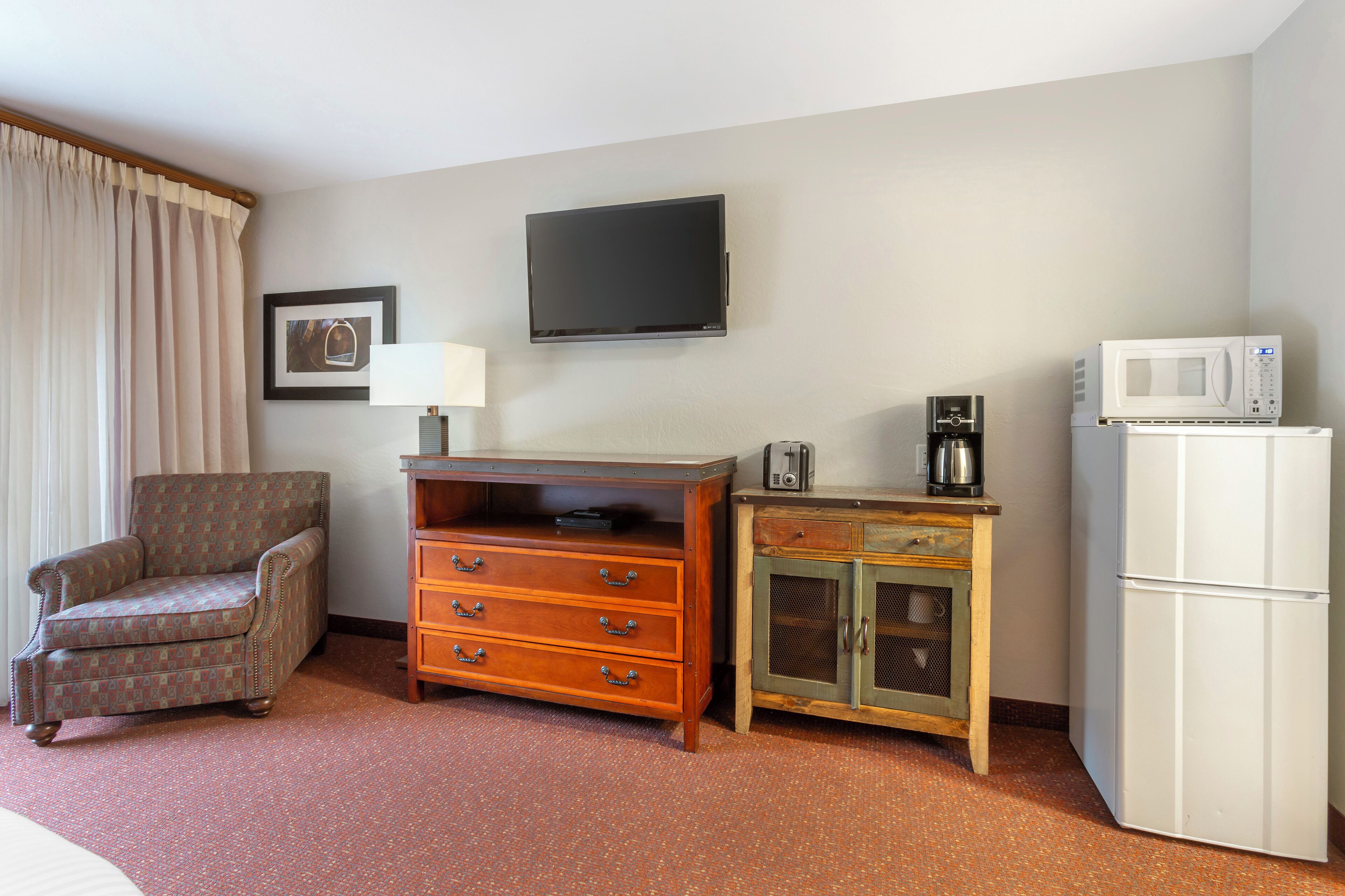 Habitación de hotel con televisión de pantalla plana, microondas, refrigerador, mueble de madera, una silla y una cama.
