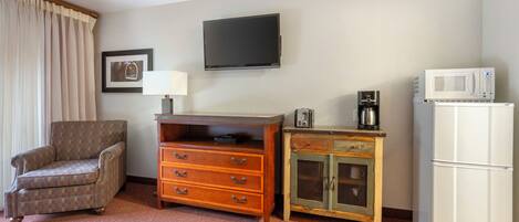 A hotel room with a flat-screen TV, a microwave, a refrigerator, a wooden cabinet, a chair, and a bed.