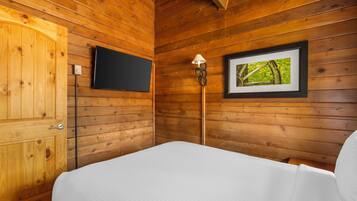 Une chambre rustique en bois avec un lit, un téléviseur fixé au mur et un tableau encadré.