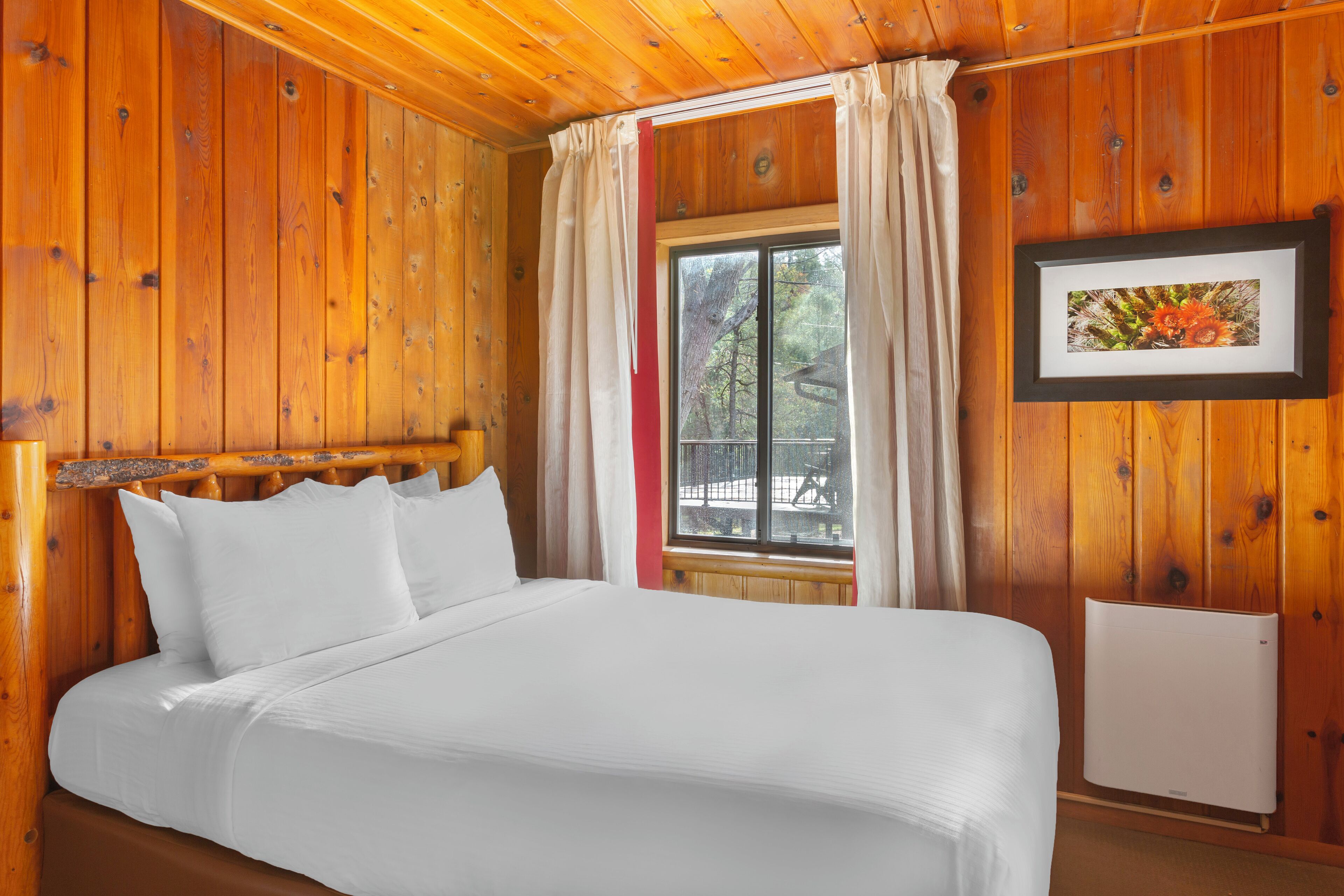 Una habitación con paneles de madera, una cama, una ventana con cortinas y un cuadro en la pared.