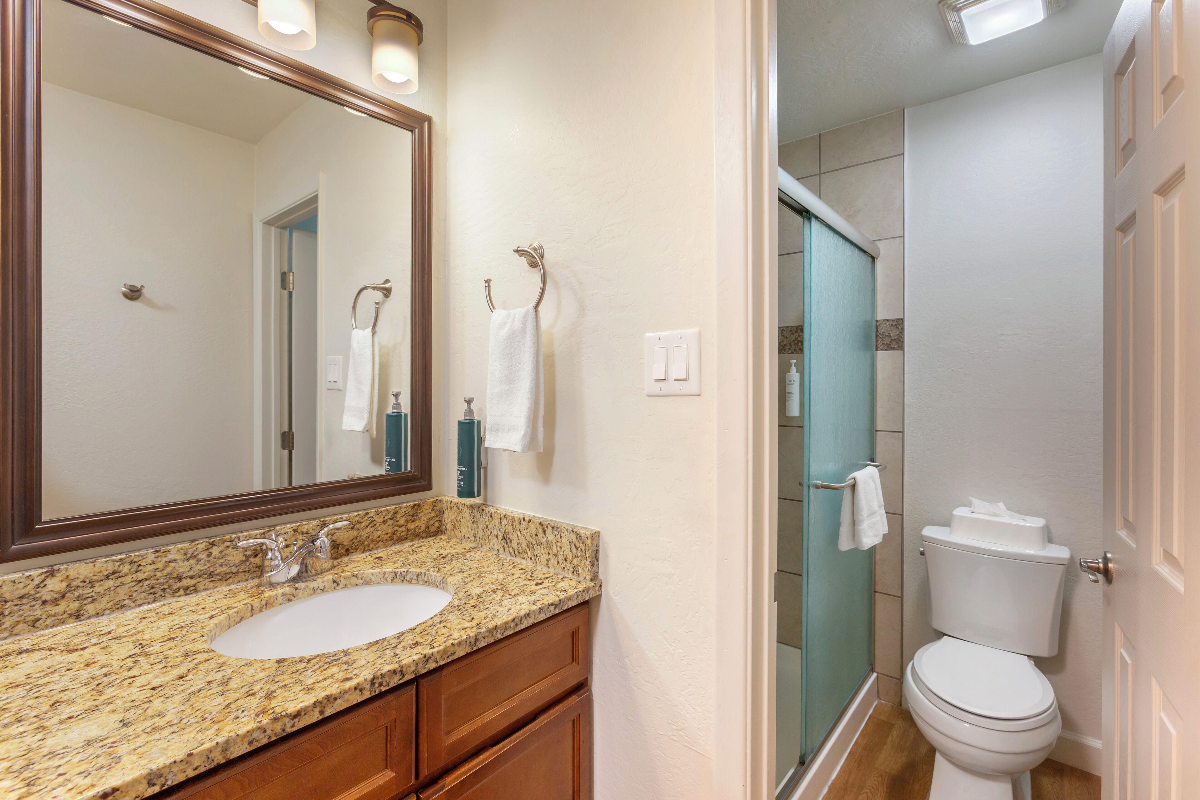 A bathroom with a granite countertop sink, a mirror, and a toilet.