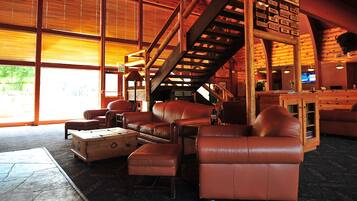 A spacious lobby with leather sofas, a wooden staircase, and large windows allowing natural light.