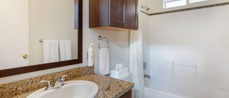 A bathroom with a granite countertop sink, a mirror, a towel rack, a toilet, and a shower area.