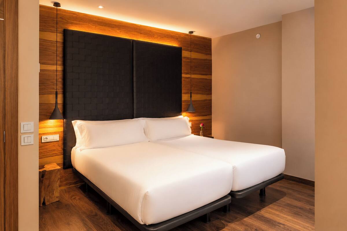 A modern hotel room with a large bed, wooden panel wall, and two pendant lights.
