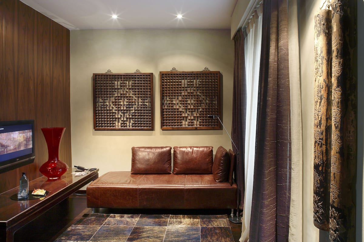 A modern living room with a brown leather sofa, a red vase, and two decorative screens on the wall.