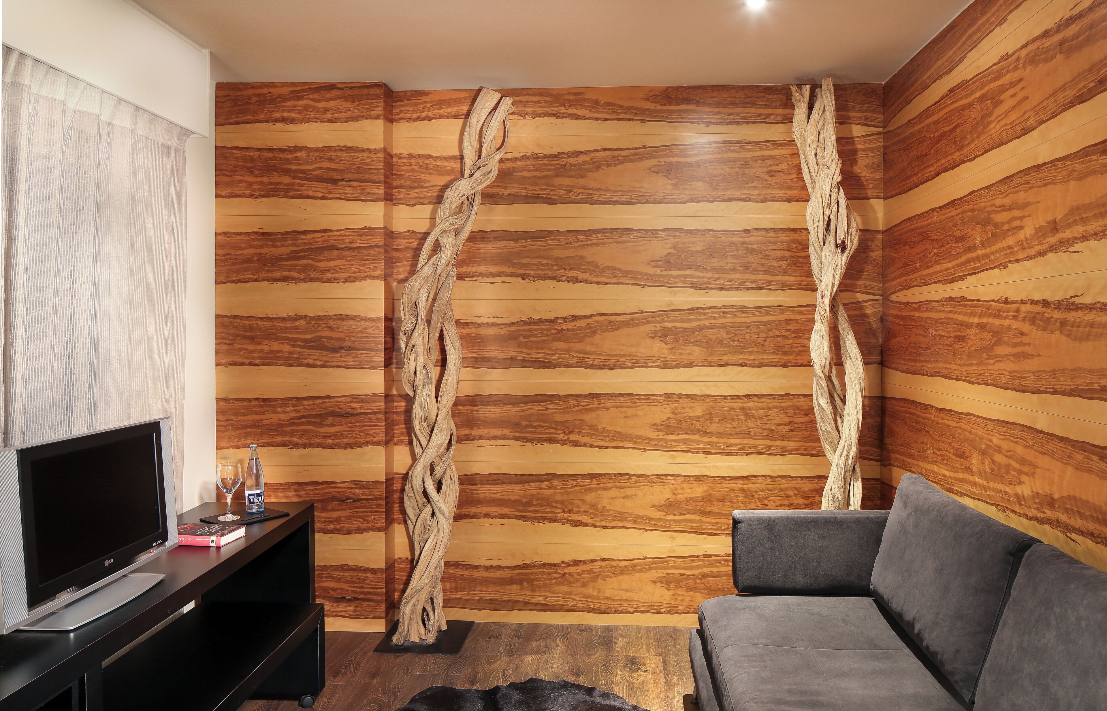 A modern living room with a wooden wall panel, a flat-screen TV, a sofa, and two abstract sculptures.