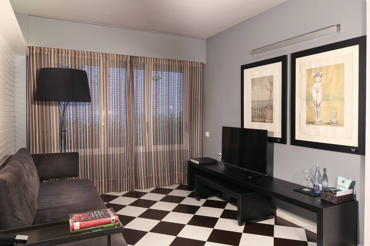 A living room with a checkered floor, a sofa, a coffee table with books, a TV, and framed artwork on the wall.