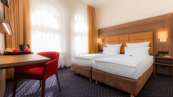 Habitación de hotel con dos camas, un escritorio con cafetera, una silla roja y una mesita de noche con teléfono.