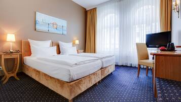 Ein Hotelzimmer mit einem großen Bett, zwei Nachttischen mit Lampen, einem Schreibtisch mit Stuhl, einem Fernseher und einem Bild an der Wand.
