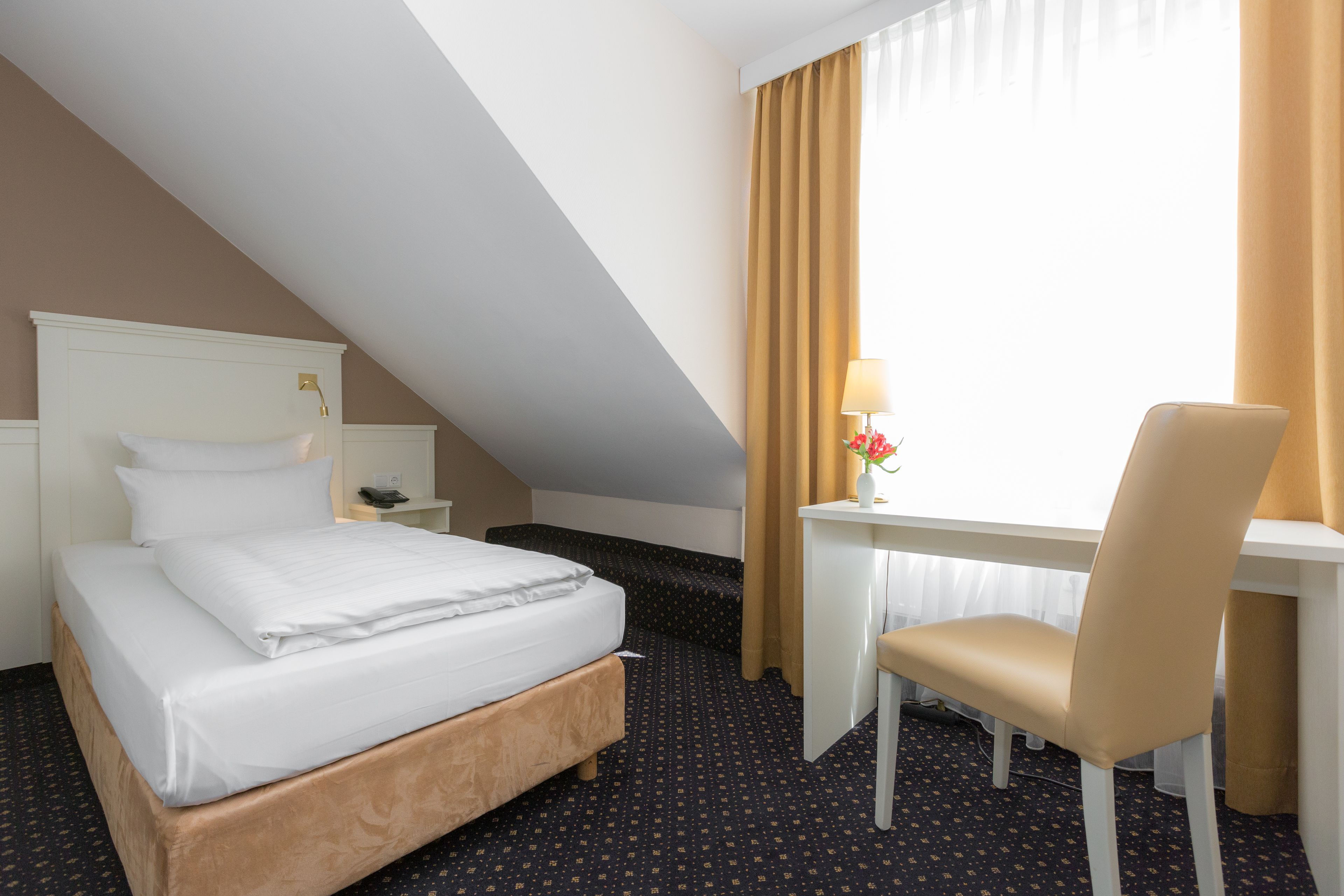 Ein Hotelzimmer mit Bett, Schreibtisch, Stuhl, Nachttisch und einem Fenster mit Vorhängen.