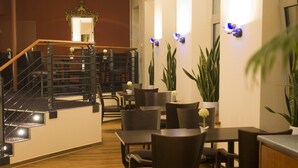 Un vestíbulo de hotel con una escalera, zona de estar y plantas decorativas.