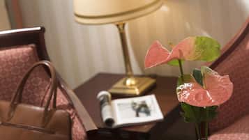 A hotel room with a bed, a bedside table with a lamp, a magazine, and a plant.