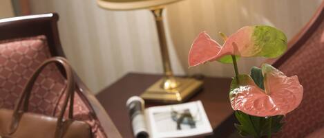 A hotel room with a bed, a bedside table with a lamp, a magazine, and a plant.
