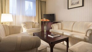 Une chambre d’hôtel avec deux canapés de couleur crème, une table basse en bois, un téléviseur et un tableau encadré au mur.