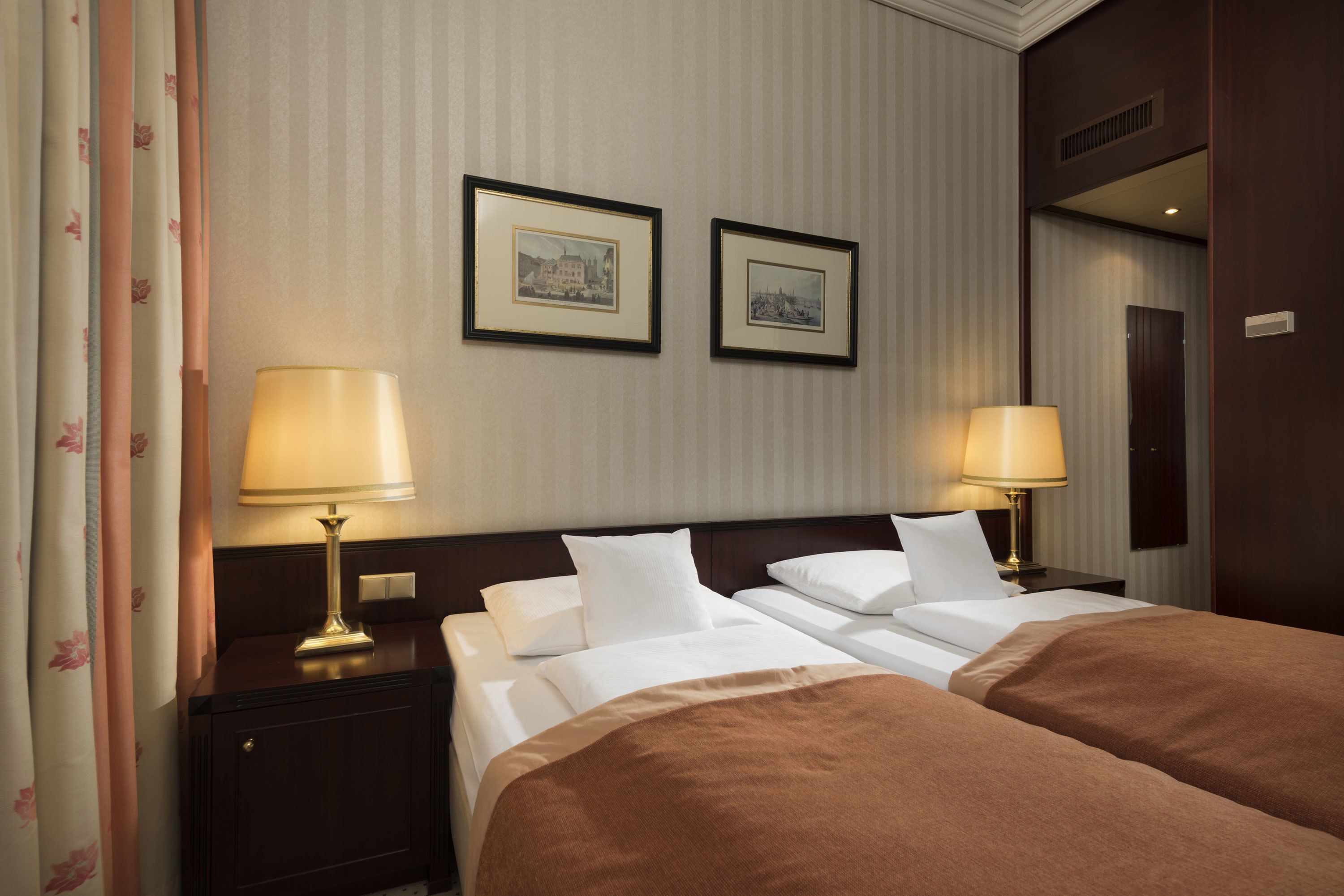 A hotel room with two beds, a nightstand with lamps, and two framed pictures on the wall.