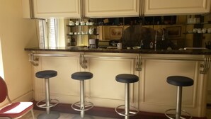 Una cocina con armarios blancos, encimera de mármol y cuatro taburetes de bar.