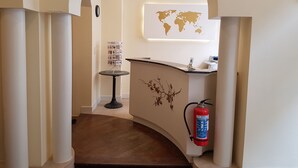 Una zona de recepción con un mapa mundial en la pared, un mostrador de recepción, una pequeña mesa con revistas y un extintor colgado en la pared.