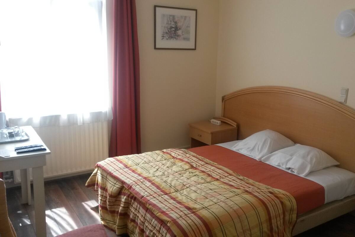 A hotel room with a bed, bedside table, and a small desk with a chair.