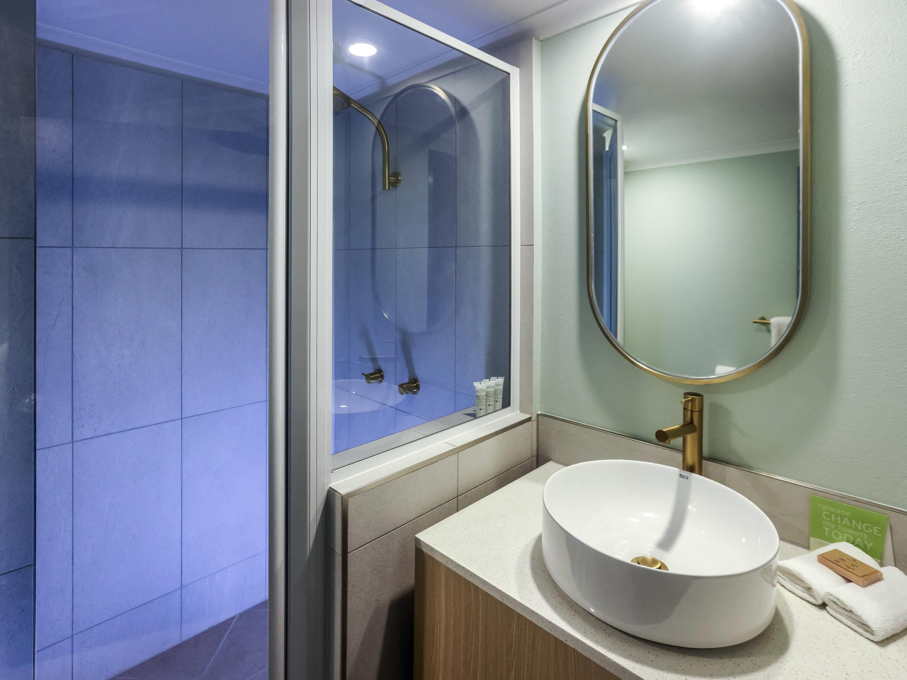 A modern bathroom with a glass shower enclosure, a round sink, and a large mirror.