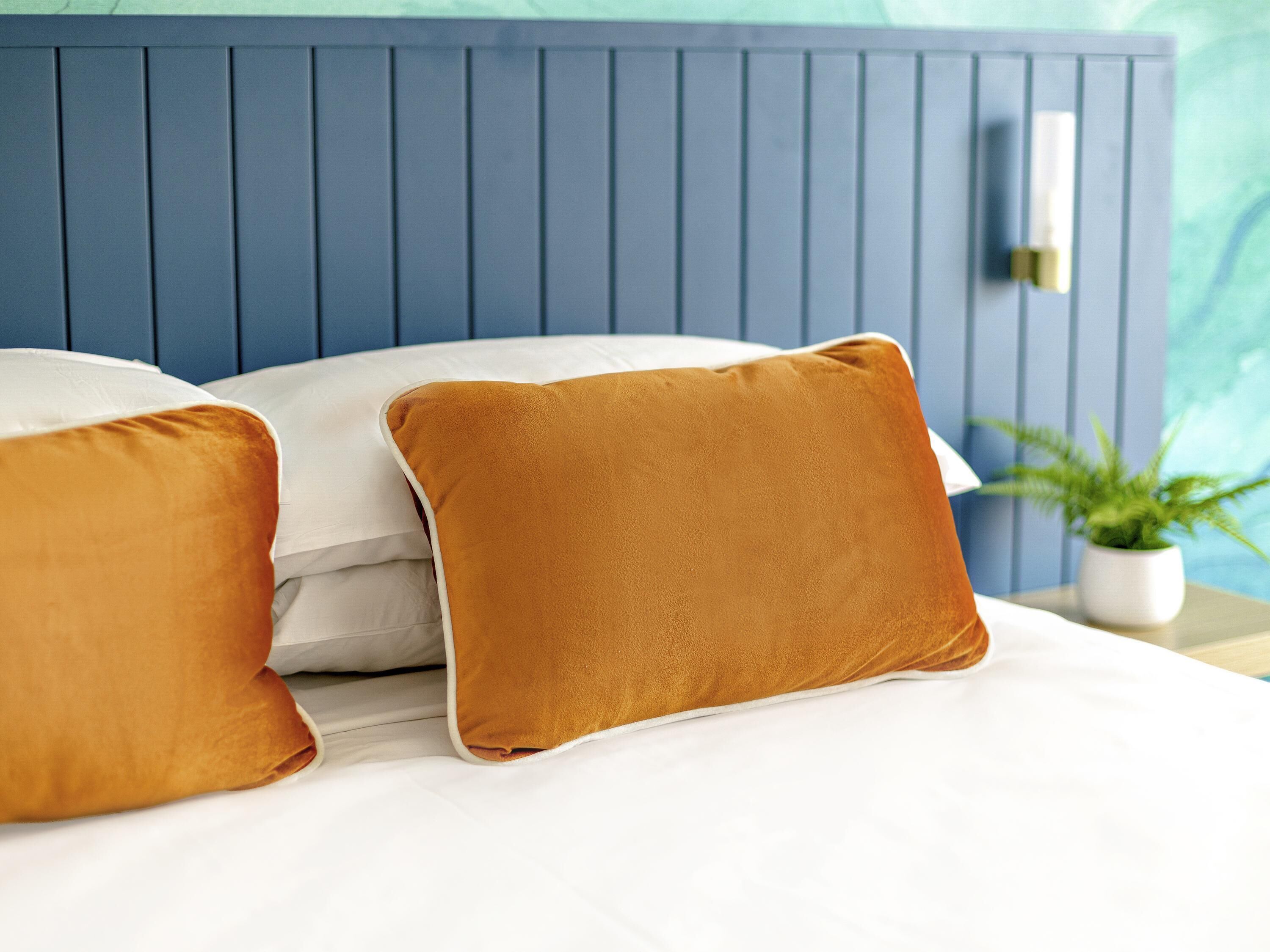A bed with white bedding and two mustard-colored pillows.