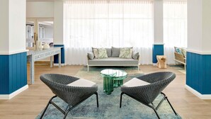 A modern living room with a sofa, two wicker chairs, a glass coffee table, and a blue accent wall. - Mercure Cairns (Cairns)